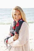 A young blonde woman by the sea wearing a light jumper and a scarf