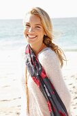 A young blonde woman by the sea wearing a light jumper and a scarf