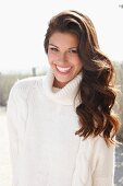 A young brunette woman outside wearing a white knitted roll-neck jumper