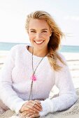 A young blonde woman by the sea wearing a light knitted jumper