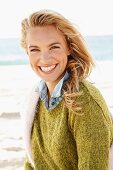 A young blonde woman by the sea wearing a knitted jumper and a denim shirt