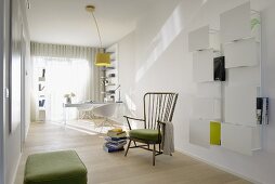 Minimalist, light-flooded study with white, wall-mounted shelves and vintage wooden armchair