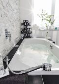 A bubble jet bathtub with underwater illumination filled with water against a natural stone wall showing a contrast between smooth and rough materials with a message in the background made from black letters