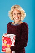 A young blonde woman holding presents and wearing a dark red jumper