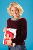 A young blonde woman holding presents and wearing a dark red jumper