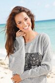 A young brunette woman by the sea wearing a grey sweatshirt