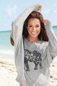 Junge, brünette Frau im grauen Sweatshirt mit Elefantenmotiv am Meer