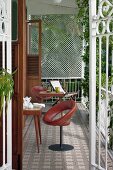 Blick durch offene Balkon Gittertüren auf gedeckte Frühstückstische im Freien, Drehstühle mit braunem Lederbezug und Tische im 50er Jahre Stil auf gemustertem Fliesenboden