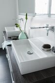 A square console basin with wall taps on a wooden washstand with drawers