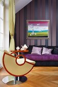 Designersessel und Beistelltisch vor lila Sofa und Bild an Streifentapete