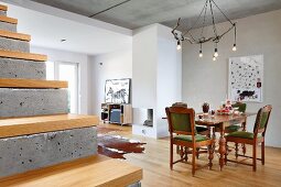 Oak furniture with turned legs and rustic light fitting made from branch in open-plan, modern interior; exposed concrete stairs with wooden treads in foreground