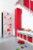 Play area; open-fronted sideboard with red storage boxes and door covered in child's drawings