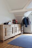 Rustikales Sideboard aus Naturholz in Dachzimmer; Kleidung aufgehängt an Metallstange und Kofferstapel im Hintergrund