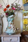 Eclectic furniture and accessories; china vase decorated with garlands and children next to wall panel with 70s floral pattern