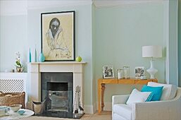 Open fireplace and white armchair in front of family photos on artistic console table against pastel wall in elegant interior