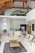 Contemporary interior with pale corner couch on tiled floor and kitchen area below gallery in converted church nave with exposed wooden roof structure