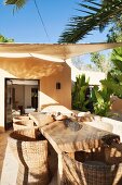 Rustic wooden table and wicker armchairs under awning on Mediterranean terrace