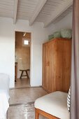 Körbe auf Holzschrank und Polsterstuhl in mediterranem Schlafzimmer mit Holzdecke