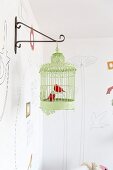 Metal bird ornaments in green vintage birdcage hanging from metal wall bracket