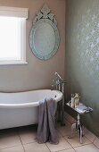 Oval mirror with ornate metal frame, vintage bathtub and floor-mounted taps in bathroom with rolled paint pattern on wall