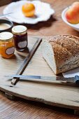 Cut loaf, knife and jars of jam on wooden board