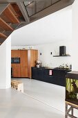 View from platform into open-plan kitchen with black base units in minimalist interior