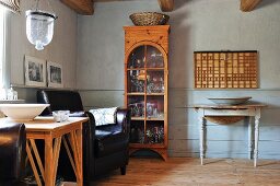 Country-house ambiance with glass-fronted cabinet, leather armchair and wooden table with turned table legs against pale grey wainscoting