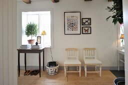 Table in front of window with plant on windowsill next to framed and mounted butterflies above pair of chairs