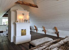 Lit candles on mantelpiece in attic bedroom with white, wood-clad walls