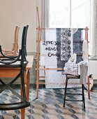 Chairs upturned on table and bar stool in front of fabric on clothes horse below window