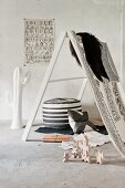 Fur and fabrics on ladder-style frame, wooden building blocks and black and white pouffe on concrete floor in loft-style interior