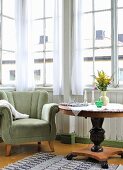 Velvet armchair and flowers on round Biedermeier table in vintage-style window bay