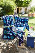Gehäkelte Decke und Kissenbezug in blau mit Blütenmuster auf antiker Bank im Garten