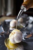 A bulb of garlic being drizzled with olive oil
