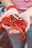 Frauenhände halten rote und orangefarbene Perlenketten