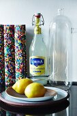 Glass swing-top bottle, colourful, rolled place mats, retro glass carafe and yellow lemons on black granite kitchen worksurface