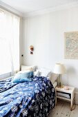 Bed with blue and white patterned bed line in corner of simple room