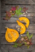 A slice and wedges of a Hokkaido pumpkin on a wooden surface with autumnal decorations