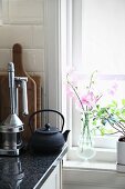 Delicate flowers and foliage plant on windowsill next to lemon press and teapot on kitchen worksurface