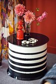 Vase of dahlias and brick-red ceramic vase on round, black and white striped coffee table in front of floral curtain