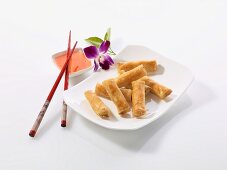 Spring rolls with chilli sauce, chopsticks and an orchid (China)