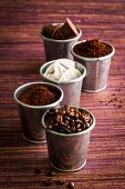 Various types of coffee: coffee beans, powder, capsules and sachets in metal cups
