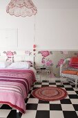 Bedroom with round rug on chequered floor, double bed with white wooden headboard and striped blanket and floral wallpaper dado