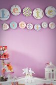 Decorative wall plates on lilac wall above bird figurines on cabinet with curved top