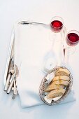 Baguettescheiben im Brotkorb, Butterdose, Besteck und Rotweinglas auf Tablett