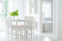 White dining room with frilled cushions on wooden chairs and crockery shelves on wall