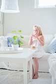 Blonde girl drinking milk on white sofa