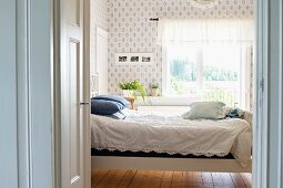 Blick durch offene Tür auf Bett mit weisser Spitzen Tagesdecke in ländlichem Ambiente