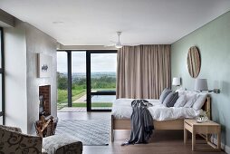 Modern bedroom with double bed opposite fireplace with firewood store; open, sliding terrace doors in background