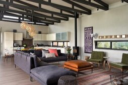 Offener Wohnraum mit Loungebereich, graues Sofa mit passendem Hocker und Leder-Couchtisch, im Hintergrund helle Einbauküche